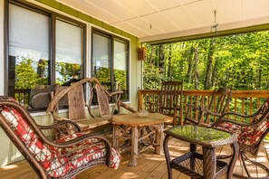 A covered outdoor seating area with wooden furniture and a view of a forest. - Expansive Deck + Covered Porch + Forest Views | 20 Min to Asheville | Ash Vale (Mars Hill)