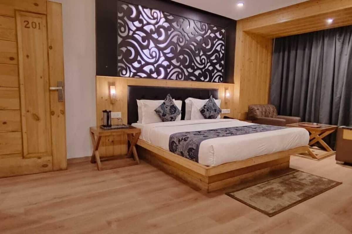 A wooden-framed bedroom with a bed, nightstands, a chair, and a window with curtains.