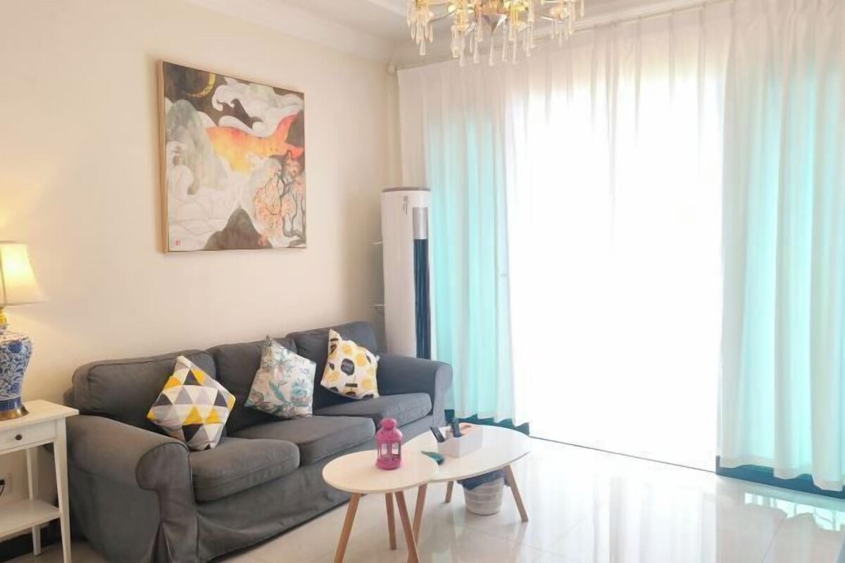 Una sala de estar moderna con un sofá gris, almohadones coloridos, una mesa de centro blanca y un cuadro abstracto grande en la pared.
