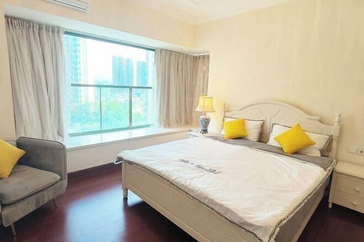A hotel room with a bed, a chair, a nightstand, a lamp, and a window with curtains.