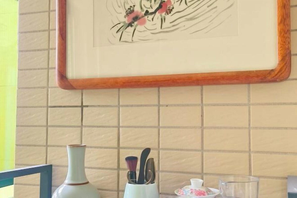 Una obra de arte enmarcada con aves en una pared, un jarrón y un recipiente con utensilios.