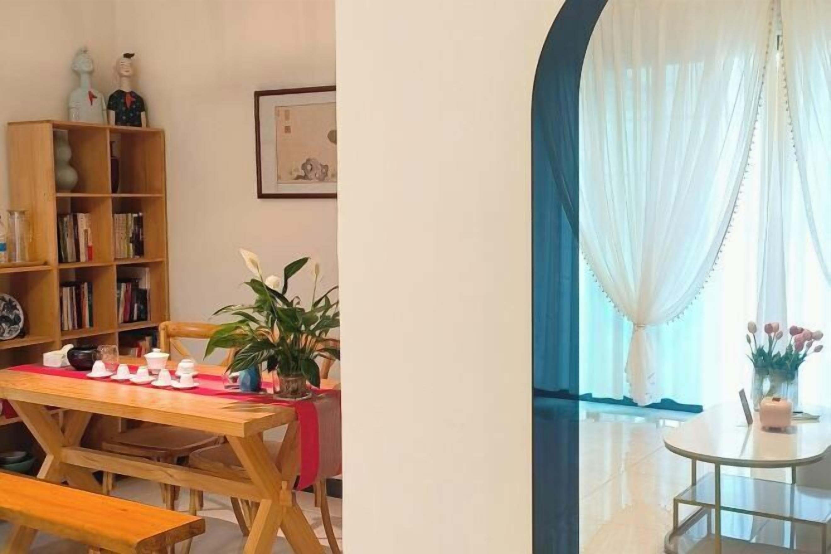 Uma área de refeições com mesa de madeira e bancos, uma estante e um vaso com planta.