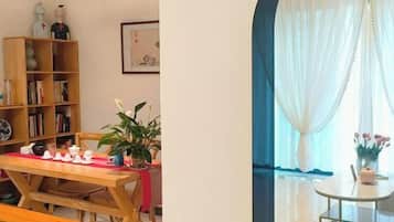 Uma área de refeições com mesa de madeira e bancos, uma estante e um vaso com planta.