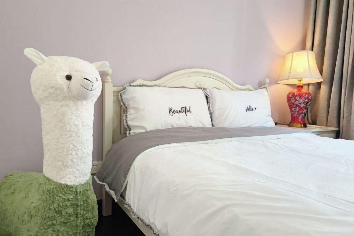 Una habitación de hotel con una cama, almohadas, una lámpara y un peluche.
