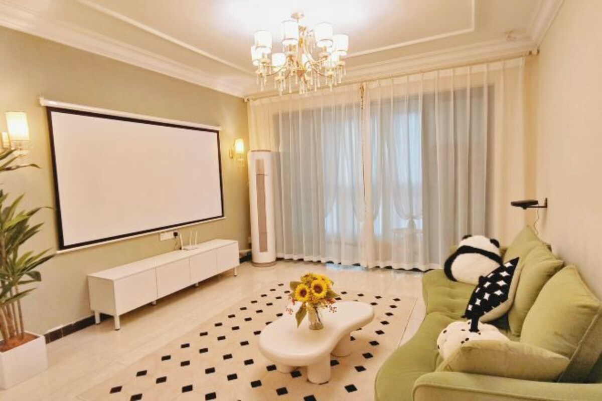 A living room with a sofa, a coffee table with a vase of flowers, a TV, and a chandelier.