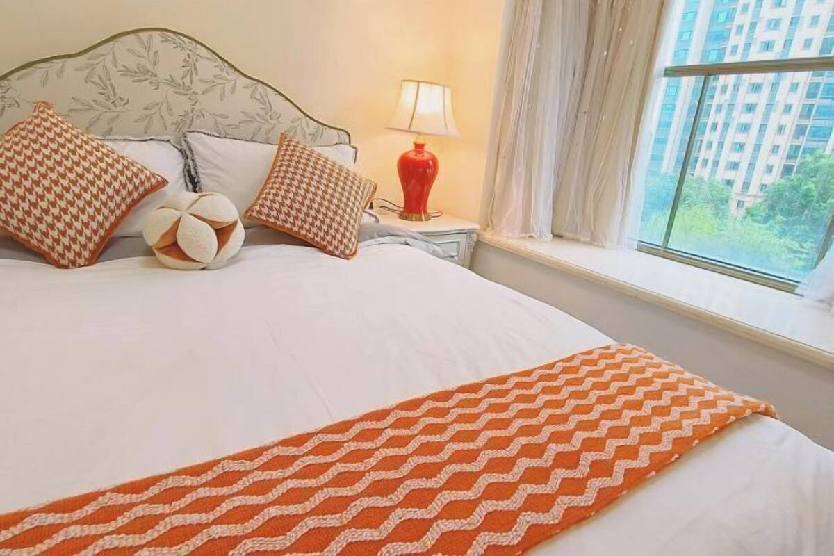 A hotel room with a bed, pillows, a lamp, and a window with a view.