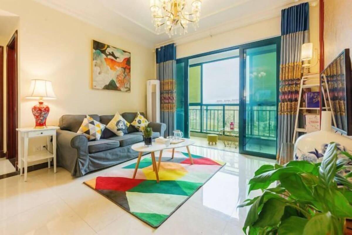 A living room with a sofa, a coffee table, a lamp, a painting, and a large window.