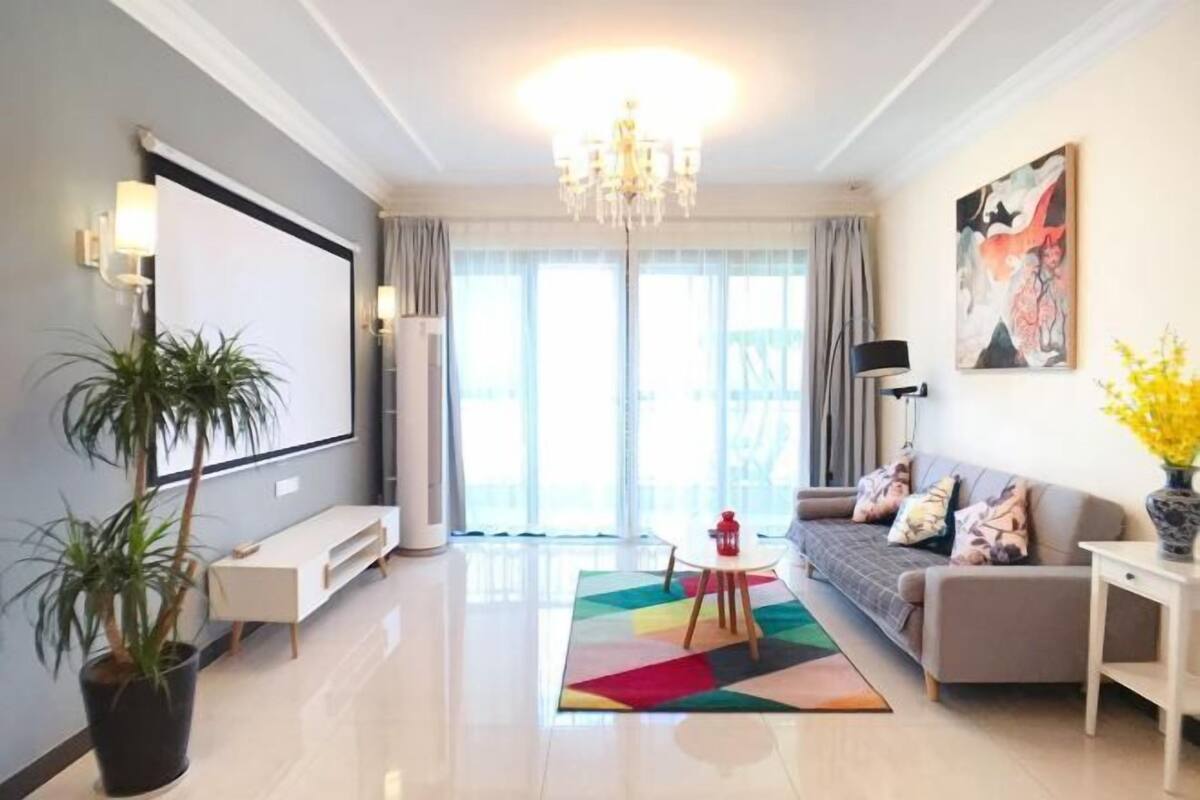 A modern living room with a sofa, a coffee table, a TV, a chandelier, and a large window.
