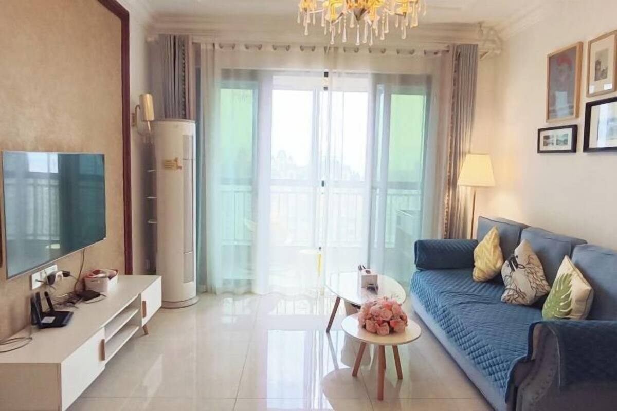 A living room with a TV, a sofa, a coffee table, and a balcony with curtains.