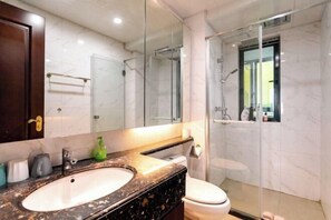 Un baño con lavamanos de mármol, inodoro, cabina de ducha de vidrio y un espejo grande.