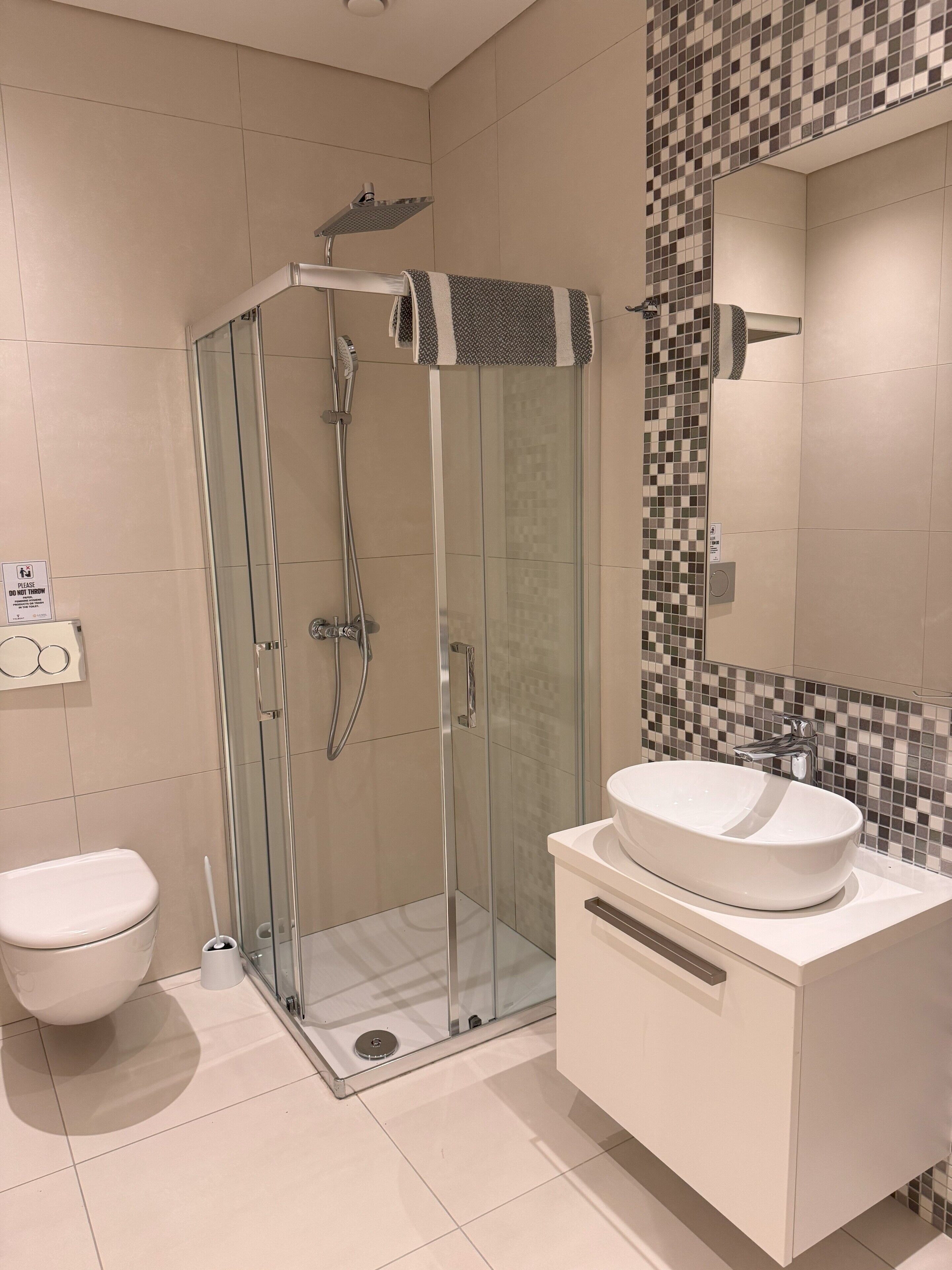 A modern bathroom with a glass-enclosed shower, a white sink, and a tiled backsplash.