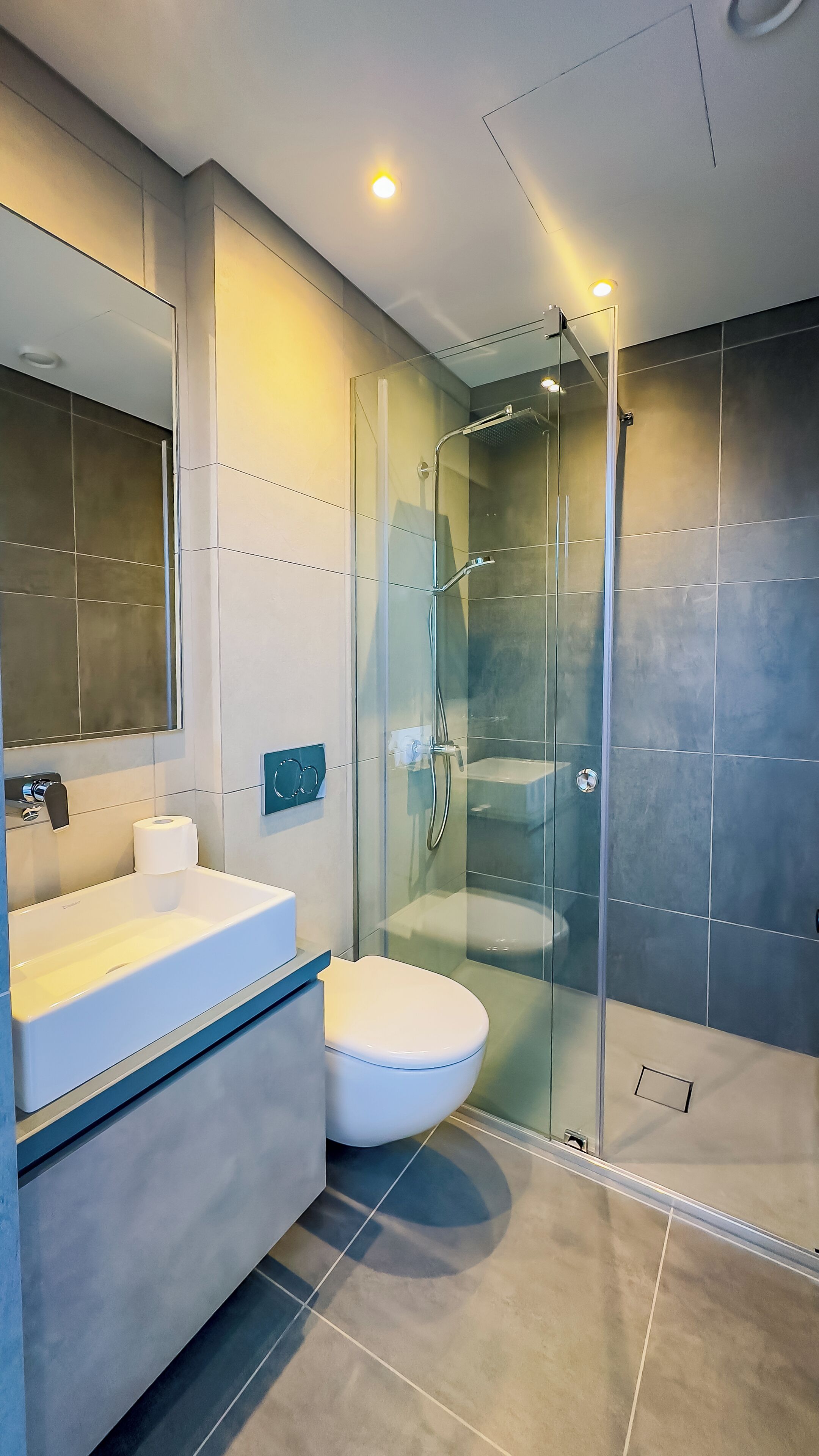 Une salle de bain moderne avec une douche à parois de verre, des toilettes blanches et un meuble-lavabo avec un miroir.