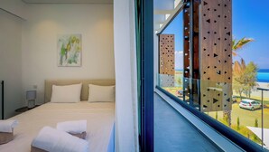 Habitación de hotel moderna con una cama grande, un cuadro en la pared y un balcón con vistas a la playa y al tráfico.
