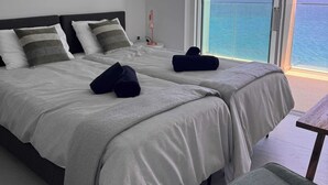 Habitación de hotel con dos camas, vista al mar y balcón.