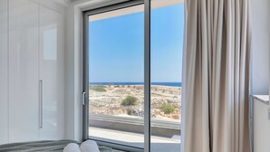 A bedroom with a large sliding glass door leading to a balcony with a view of rocky terrain and the sea. - Sea Pearl Beachfront Villa (Ayia Napa)