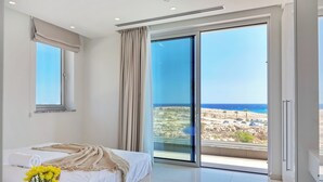 A modern bedroom with a large bed, a view of the sea, and a sliding glass door to the balcony. - Sea Pearl Beachfront Villa (Ayia Napa)