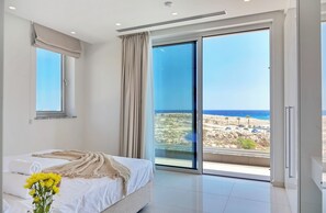 A bedroom with a bed, a window, and a view of the sea.