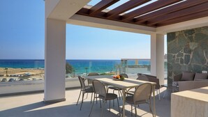 A modern outdoor dining area with a view of the ocean, a stone wall, and a pergola. - Sea Pearl Beachfront Villa (Ayia Napa)