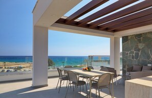 A modern outdoor dining area with a view of the ocean, a stone wall, and a pergola.