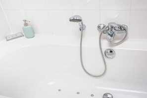 Une baignoire blanche équipée d’un pommeau de douche à main, d’un flexible de douche et d’un pommeau de douche à main avec un tuyau flexible.