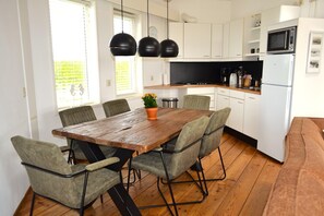 A modern kitchen with white cabinets, a wooden dining table, and a built-in oven.
