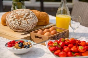 Une table dressée pour le petit-déjeuner avec du pain, des œufs, des fraises et du jus d’orange.