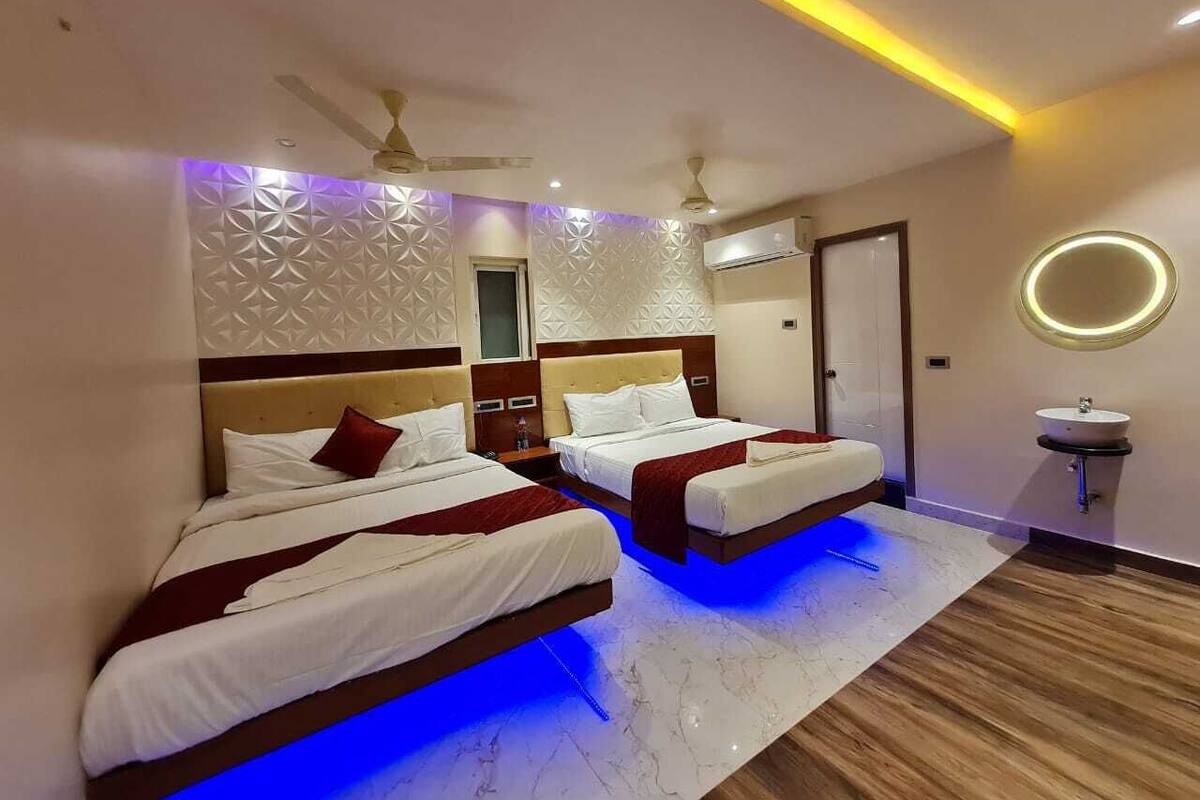 Habitación de hotel con dos camas, ventilador de techo, aire acondicionado de pared y lámpara circular.