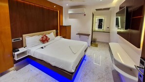 A modern hotel room with a large bed, a built-in TV, a vanity with a mirror, and a ceiling fan. - Hotel Sannidhi (Vijayawada)