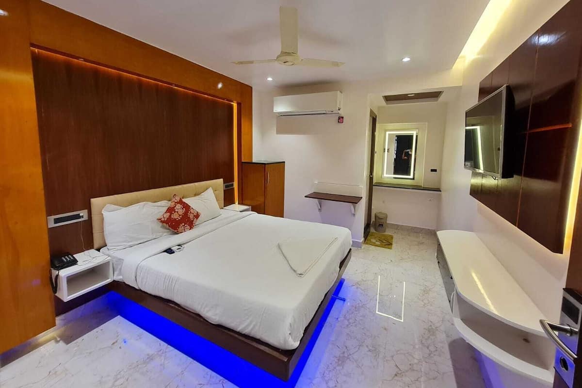 Una habitación de hotel moderna con una cama grande, un televisor integrado, un tocador con espejo y un ventilador de techo.