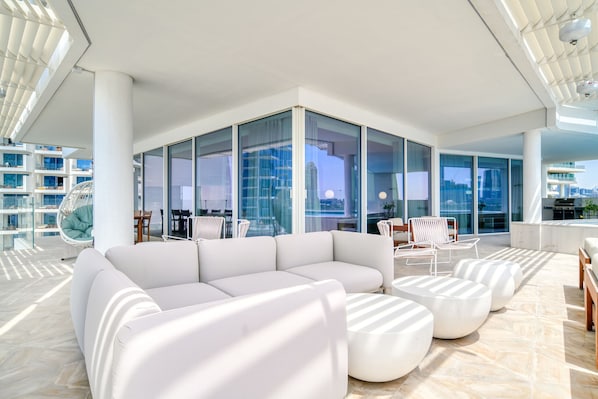 A modern, spacious lounge area with a white sectional sofa, round ottomans, and a glass-enclosed seating area with chairs.
