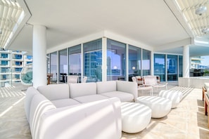 A modern, spacious lounge area with a white sectional sofa, round ottomans, and a glass-enclosed seating area with chairs.