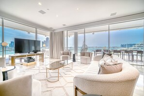 Una sala de estar moderna con un televisor grande, asientos cómodos y vistas a la ciudad y al agua.