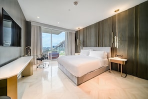 A modern hotel room with a large bed, a desk, and a view of the cityscape.