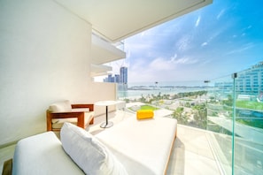A balcony with a bed, a small table, and a view of a cityscape and water.