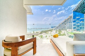 A balcony with a view of a coastal cityscape, a wooden chair, a small table, and a bed with a yellow pillow. - FIVE Palm Jumeirah: 4BR Penthouse w/ Private Pool (Dubai)
