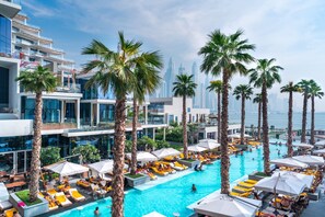 A rooftop pool area with multiple levels of balconies, palm trees, and a view of the city skyline.