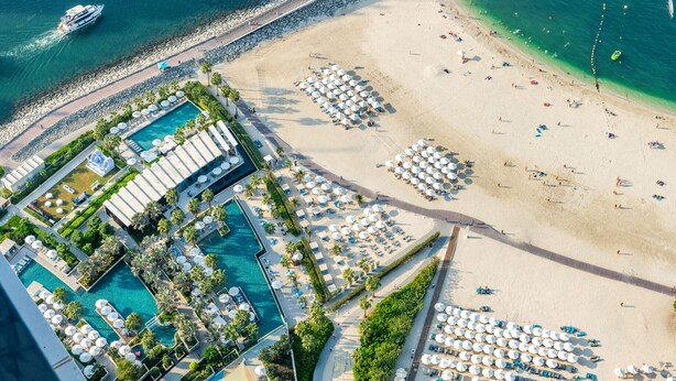 An aerial view of a resort with multiple swimming pools, beach areas, and numerous umbrellas.