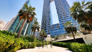 A modern high-rise building with a distinctive arch design, surrounded by palm trees and greenery.