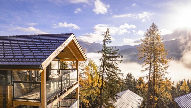 A wooden cabin with a glass balcony overlooking a forested mountain area. - Superior Chalet III with Sauna & Hot Tub (Turrach)