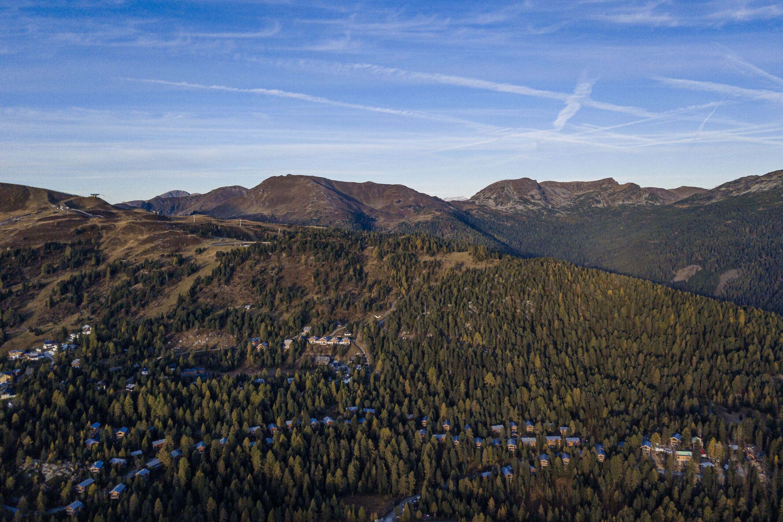 A mountainous landscape with a small settlement of houses surrounded by dense forest.
