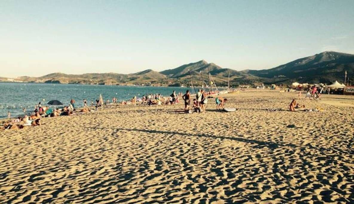 Ein Strand mit Menschen, Zelten und Bergen im Hintergrund.