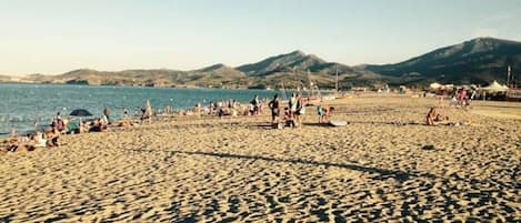 A beach with people, tents, and mountains in the background.