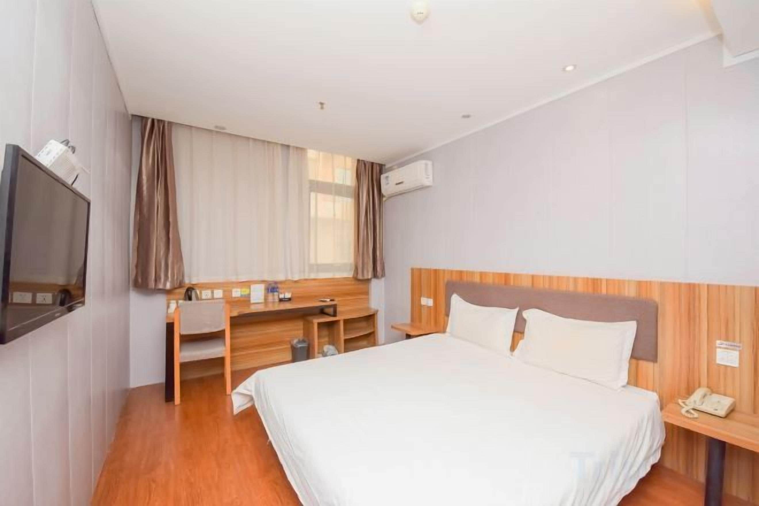 Une chambre d’hôtel avec un lit, un bureau, une télévision et une fenêtre avec des rideaux.