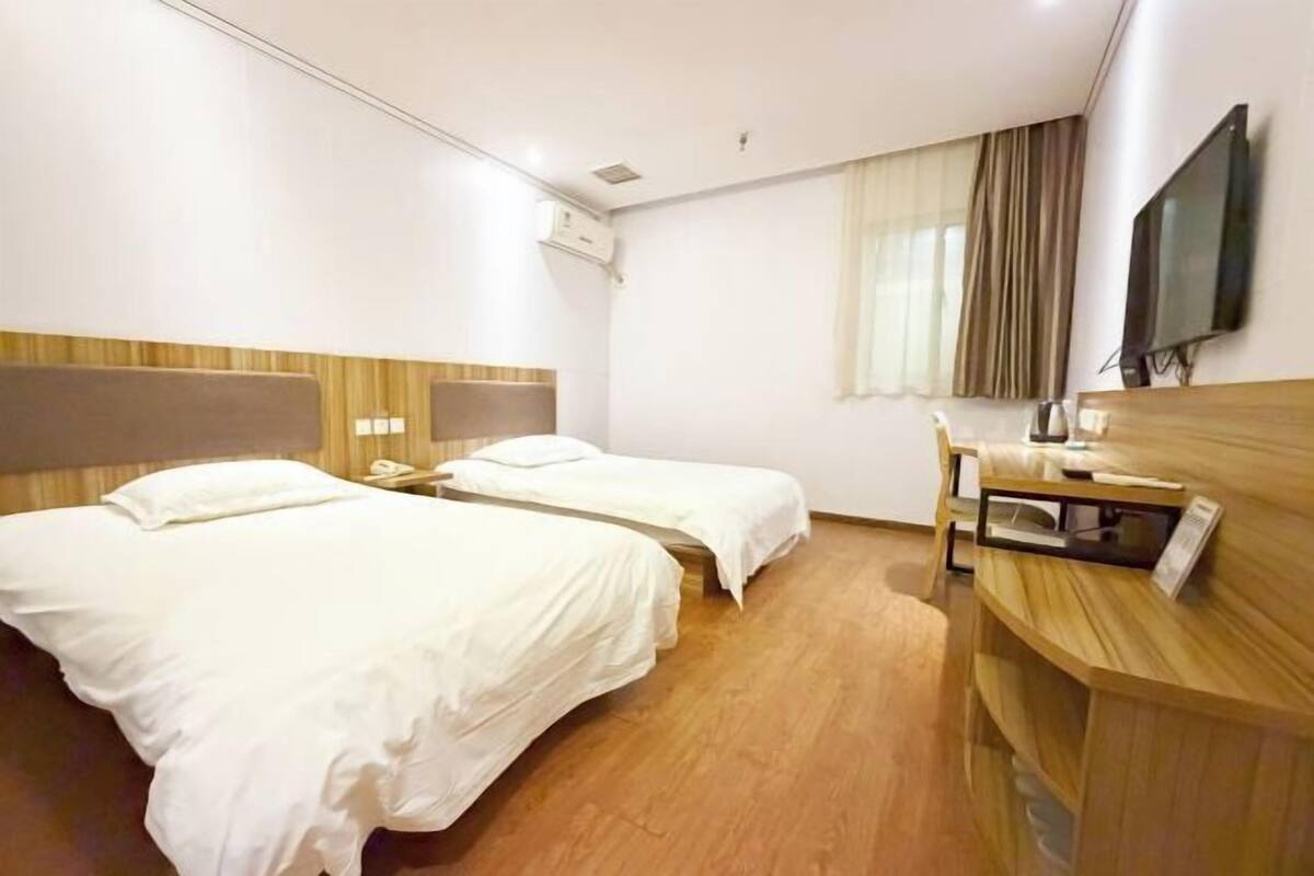 Ein Hotelzimmer mit zwei Betten, einem Schreibtisch, einem Stuhl, einem Flachbildfernseher und einer Klimaanlage.