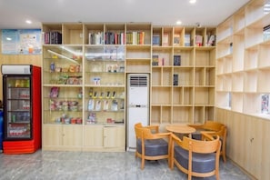 A library with bookshelves, a vending machine, and a table with chairs. - Meet Maple Hotel (Shijiazhuang)