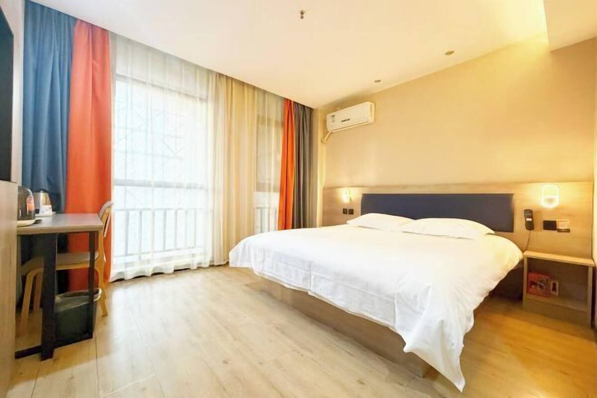 Ein Hotelzimmer mit Bett, Schreibtisch, Stuhl, Nachttisch und einem Fenster mit Vorhängen.