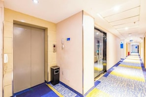 Un couloir d’hôtel avec un ascenseur, une poubelle et une porte en verre.