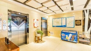 An elevator with a digital display, a reception desk, a vending machine, and informational posters on the wall. - Meet Maple Hotel (Shijiazhuang)