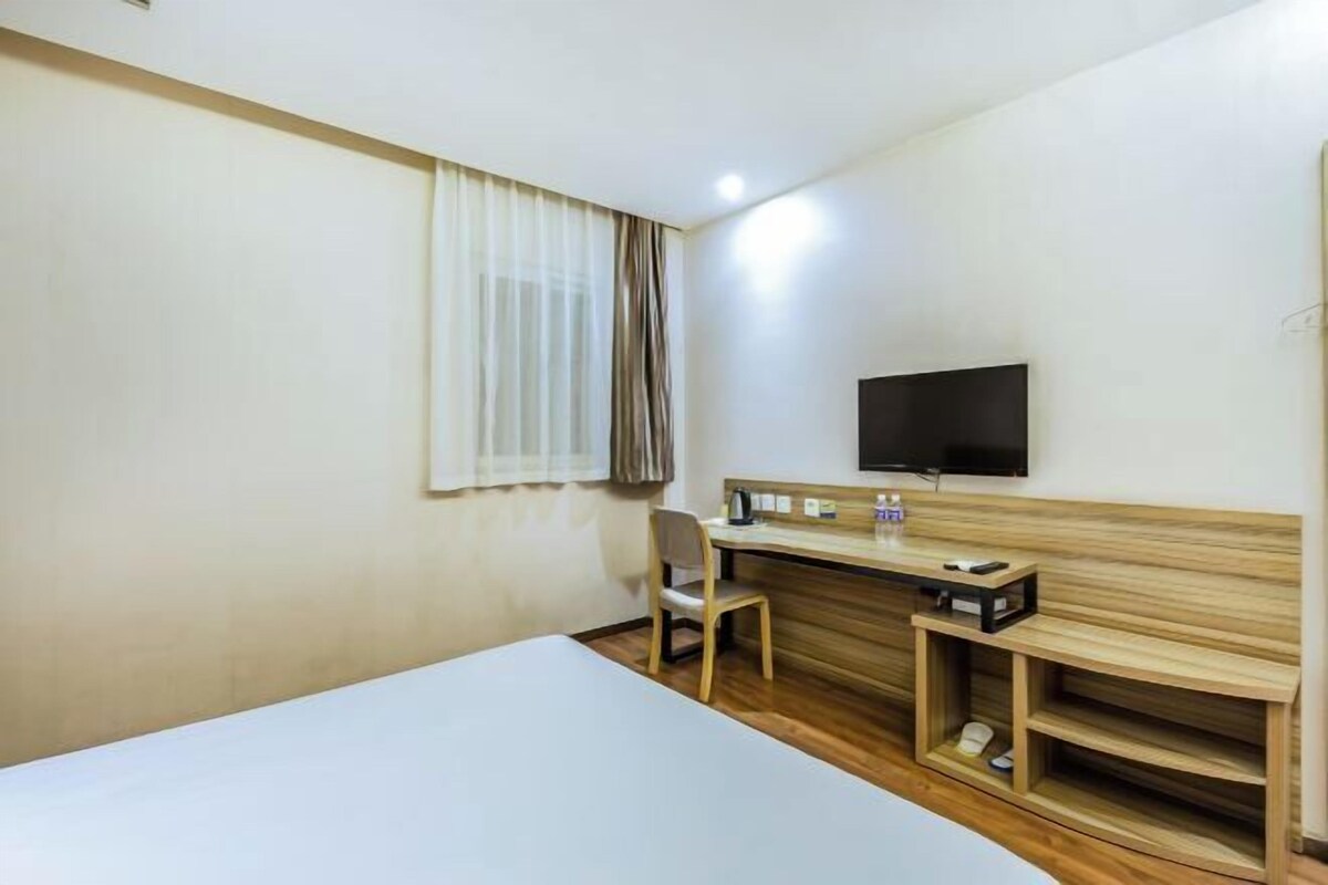 Hotellihuone, jossa on sänky, työpöytä, tuoli, televisio ja kenkäteline.