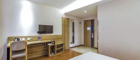 A hotel room with a bed, a desk with a chair, a television mounted on the wall, and a wooden floor.